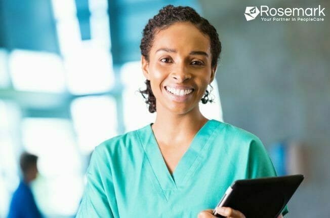 Smiling private duty home care caregiver in green scrubs holding a mobile tablet device