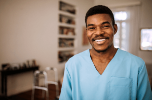 Male caregiver in blue scrubs standing in a client's home