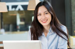 woman in blue shirt with dark-colored hair smiling while using her computer to make a home care software transition