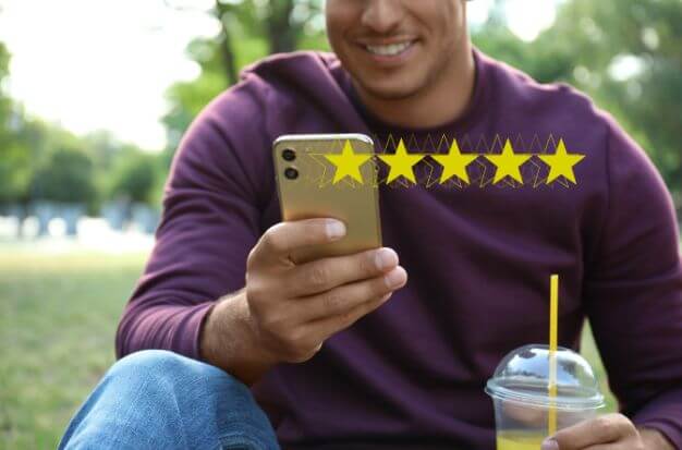 Man in a purple shirt holding a cell phone that is superimposed with 5 yellow stars showing he provided positive client reviews