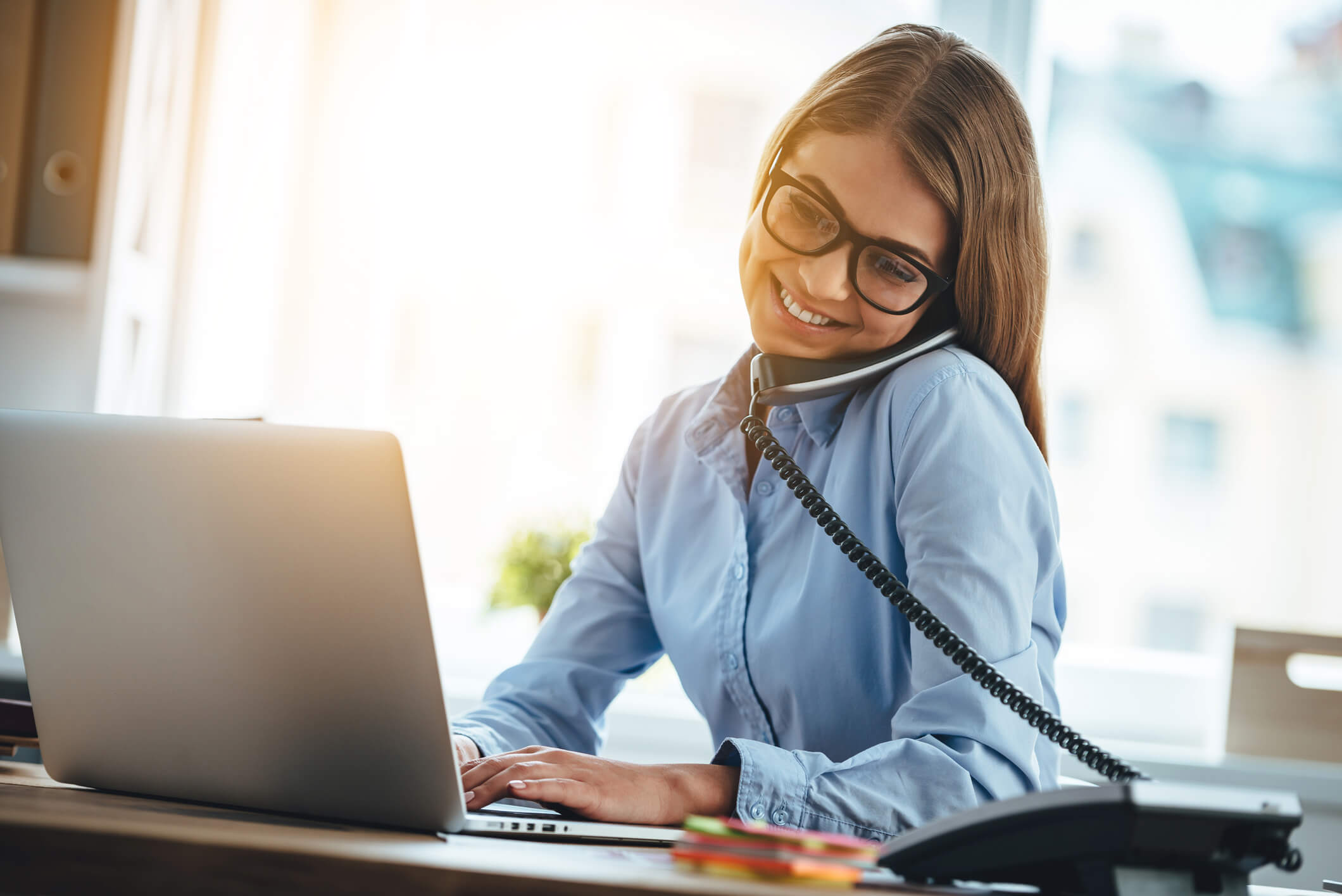 A home care sales professional smiles and types on her computer as she talks on the phone.