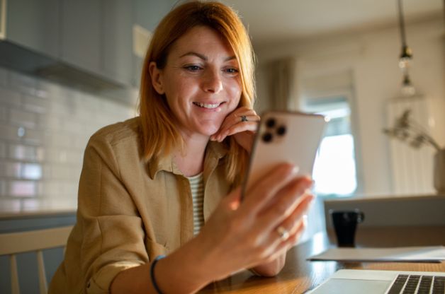 A woman smiles as she engages on social media platforms on her phone.