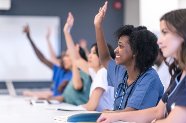 Caregivers in scrubs raising their hands during a caregiver training session in a classroom setting