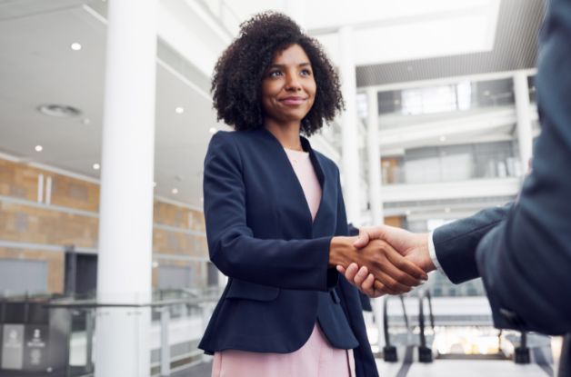 A home care professional shaking hands with a business partner inside a corporate atrium to build a referral partnership network.